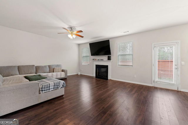 living room featuring dark wood-style floors, baseboards, visible vents, and a glass covered fireplace