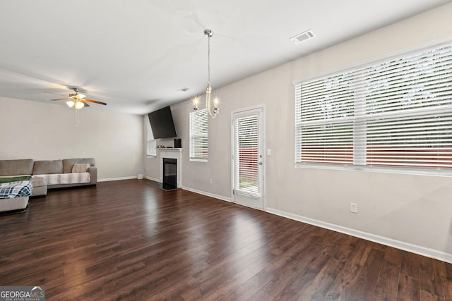 unfurnished living room with visible vents, dark wood finished floors, baseboards, a glass covered fireplace, and ceiling fan with notable chandelier