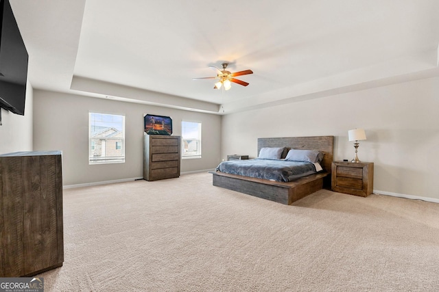 bedroom with a ceiling fan, a tray ceiling, light carpet, and baseboards