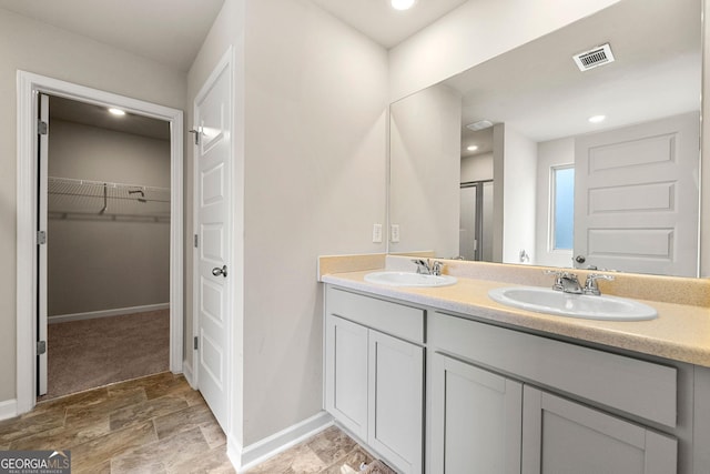 bathroom featuring a sink, double vanity, a walk in closet, and visible vents