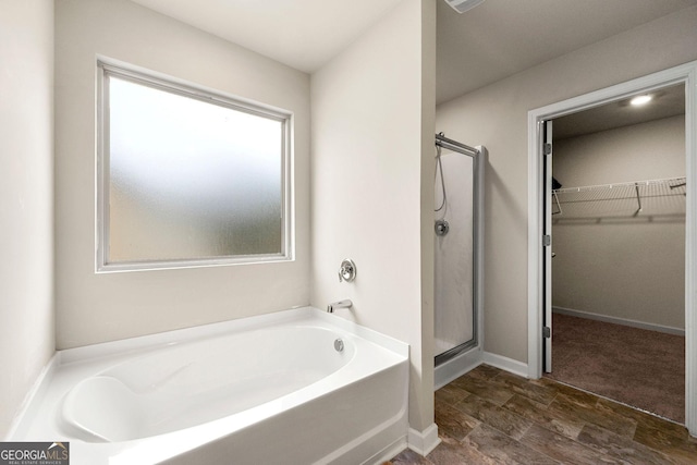 full bath featuring a walk in closet, a garden tub, a shower stall, and baseboards