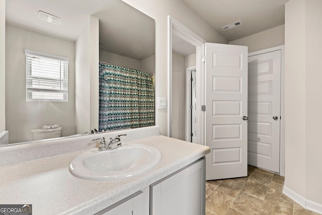 bathroom featuring toilet, vanity, visible vents, baseboards, and stone finish floor