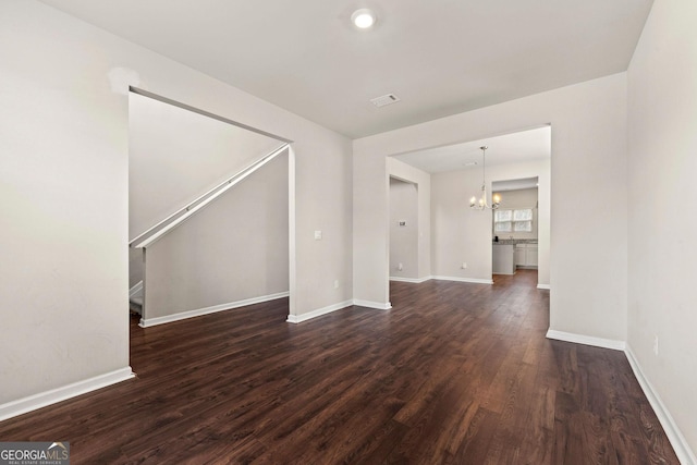 unfurnished living room with baseboards, dark wood finished floors, and a notable chandelier