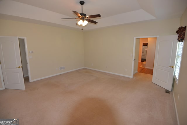 unfurnished bedroom with light carpet, baseboards, visible vents, a raised ceiling, and ceiling fan