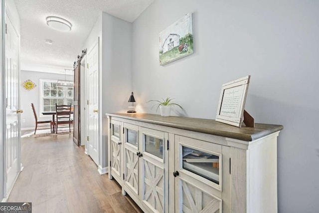 hallway with a barn door, a textured ceiling, baseboards, and wood finished floors