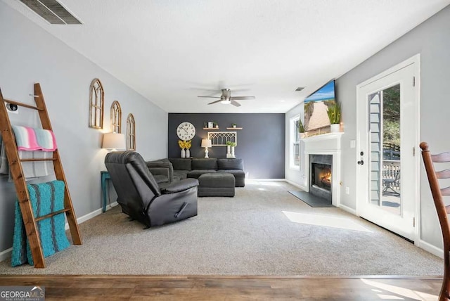 carpeted living area with visible vents, a fireplace with flush hearth, ceiling fan, wood finished floors, and baseboards