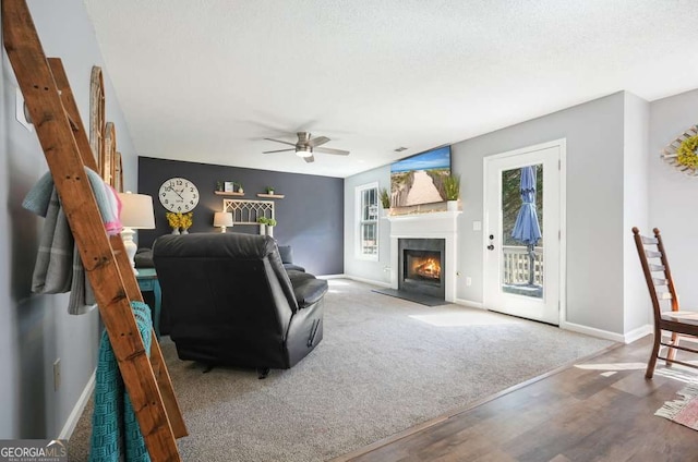 living area with a fireplace with flush hearth, baseboards, a ceiling fan, and wood finished floors