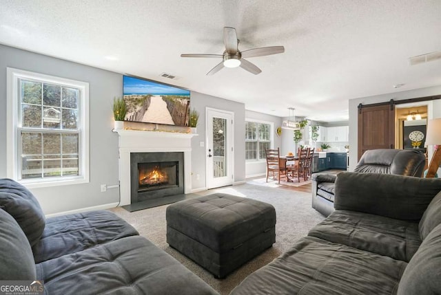 living room with carpet floors, a barn door, visible vents, and a ceiling fan