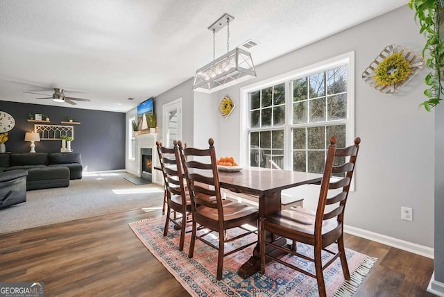 dining area featuring a warm lit fireplace, baseboards, visible vents, and dark wood finished floors