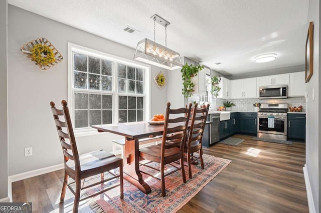 dining space featuring dark wood-type flooring, visible vents, a textured ceiling, and baseboards