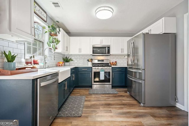 kitchen featuring white cabinets, blue cabinets, stainless steel appliances, and light countertops