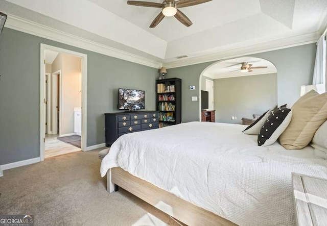 bedroom with crown molding, arched walkways, a tray ceiling, and light colored carpet