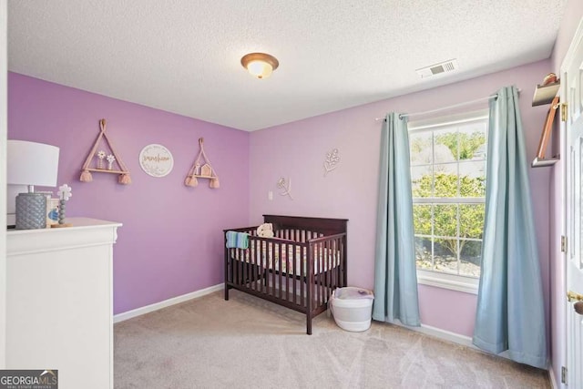 bedroom with a textured ceiling, light carpet, visible vents, baseboards, and a nursery area