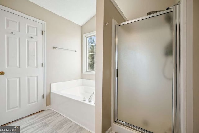 bathroom with lofted ceiling, wood finished floors, a stall shower, and a garden tub