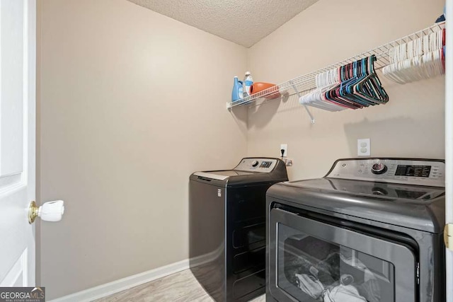 washroom with a textured ceiling, wood finished floors, laundry area, independent washer and dryer, and baseboards