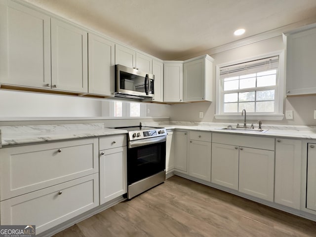 kitchen with stainless steel appliances, white cabinets, a sink, and light stone counters