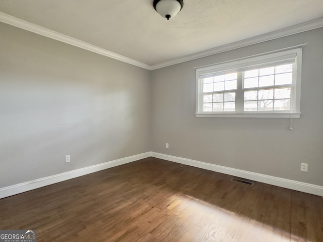 empty room with crown molding, dark wood finished floors, visible vents, and baseboards