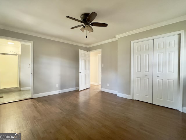 unfurnished bedroom featuring baseboards, ceiling fan, dark wood-type flooring, crown molding, and a closet