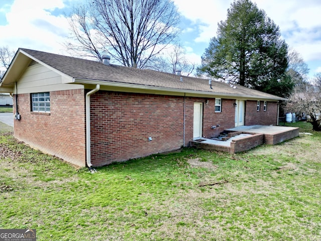 back of property featuring roof with shingles, brick siding, a lawn, and a patio