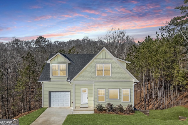 view of front of property with a garage, concrete driveway, roof with shingles, and a yard