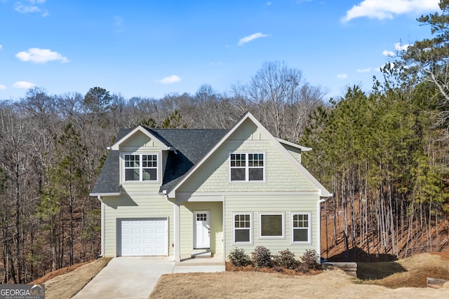 view of front of property featuring driveway, a shingled roof, a garage, and a wooded view