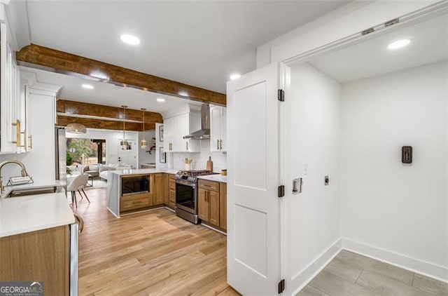 kitchen featuring light countertops, wall chimney range hood, stainless steel range with gas cooktop, black microwave, and a sink