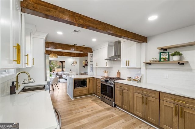 kitchen with stainless steel range with gas stovetop, white cabinetry, built in microwave, beamed ceiling, and wall chimney exhaust hood