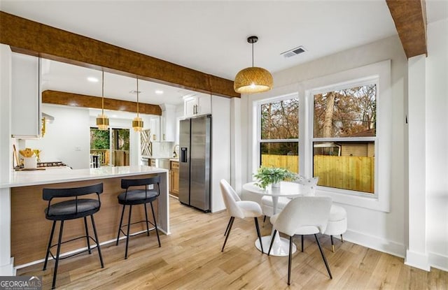 kitchen with light countertops, stainless steel fridge with ice dispenser, decorative light fixtures, and white cabinets