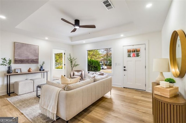 living room with light wood-type flooring, visible vents, a tray ceiling, and recessed lighting