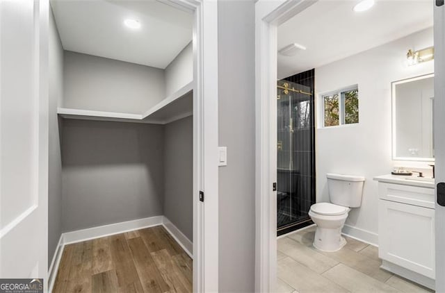 bathroom featuring toilet, a shower stall, baseboards, and vanity