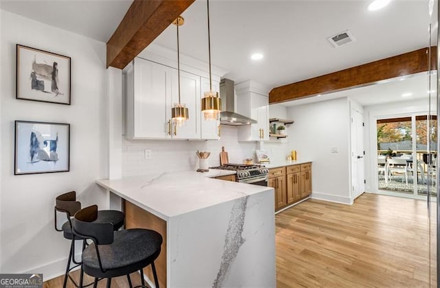 kitchen featuring white cabinets, wall chimney range hood, beamed ceiling, gas stove, and decorative light fixtures