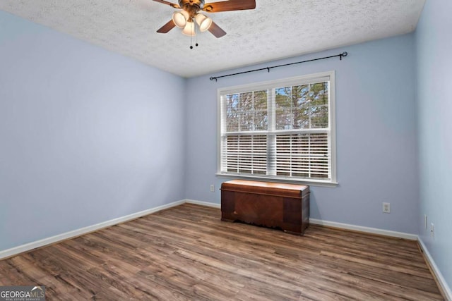 empty room featuring a textured ceiling, wood finished floors, a ceiling fan, and baseboards