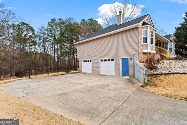 view of property exterior featuring an attached garage, a chimney, fence, and concrete driveway