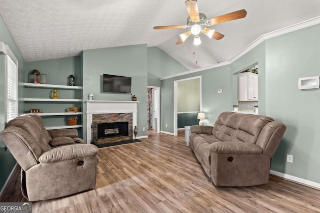 living room with baseboards, light wood-style flooring, vaulted ceiling, crown molding, and a stone fireplace