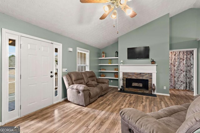 living room featuring vaulted ceiling, a stone fireplace, a textured ceiling, and wood finished floors