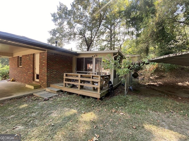 back of house featuring entry steps, a sunroom, an attached carport, a wooden deck, and brick siding