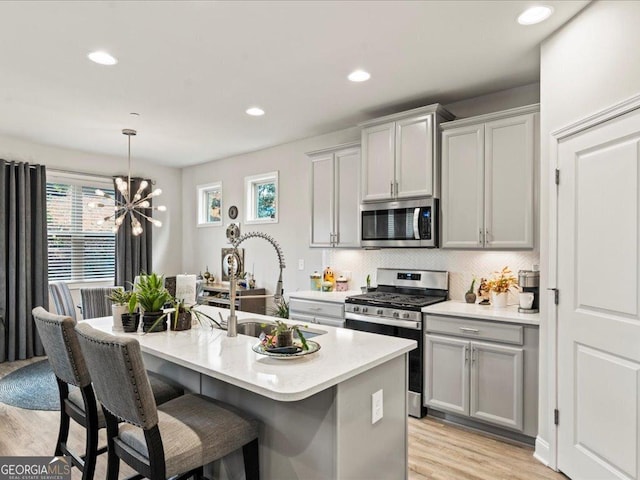 kitchen with light wood finished floors, appliances with stainless steel finishes, a sink, light countertops, and backsplash