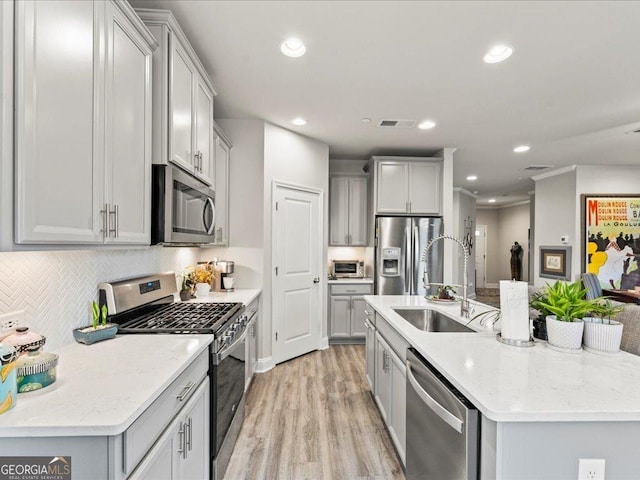 kitchen with visible vents, a kitchen island with sink, gray cabinets, stainless steel appliances, and a sink