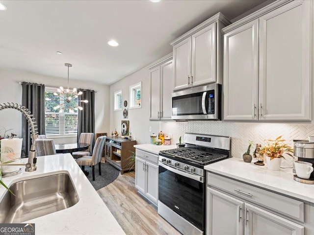 kitchen featuring stainless steel appliances, tasteful backsplash, light wood-style floors, a sink, and a chandelier