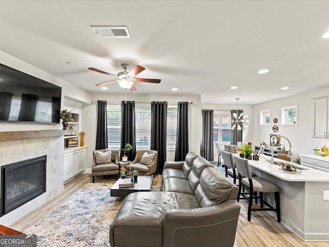 living room with light wood finished floors, recessed lighting, visible vents, and a glass covered fireplace