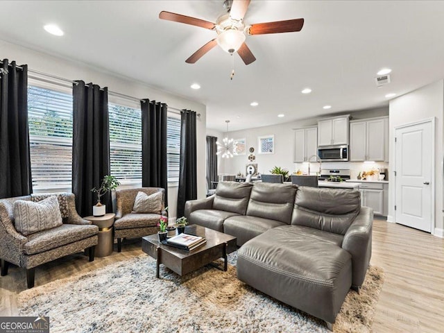 living room with light wood-style flooring, ceiling fan with notable chandelier, visible vents, and recessed lighting