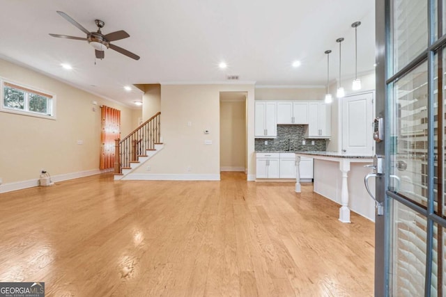 kitchen featuring a breakfast bar area, white cabinetry, open floor plan, hanging light fixtures, and an island with sink