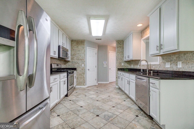 kitchen featuring stainless steel appliances, dark countertops, a sink, and white cabinetry