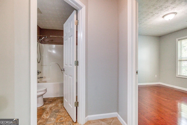 bathroom featuring baseboards, toilet, a textured ceiling, and shower / tub combination