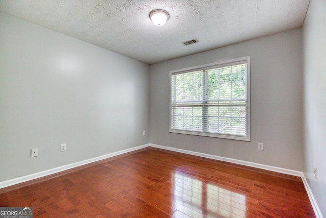 unfurnished room with visible vents, a textured ceiling, baseboards, and wood finished floors