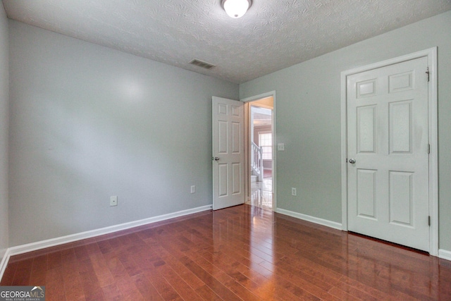 unfurnished bedroom with visible vents, a textured ceiling, baseboards, and dark wood-style flooring