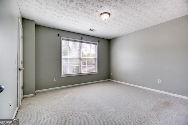 spare room with light carpet, baseboards, visible vents, and a textured ceiling