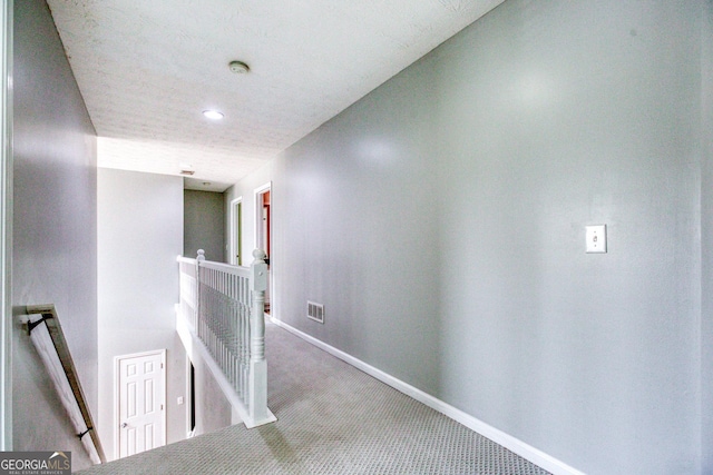 corridor featuring carpet floors, visible vents, a textured ceiling, an upstairs landing, and baseboards