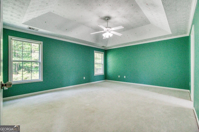 empty room with carpet floors, visible vents, baseboards, a tray ceiling, and crown molding