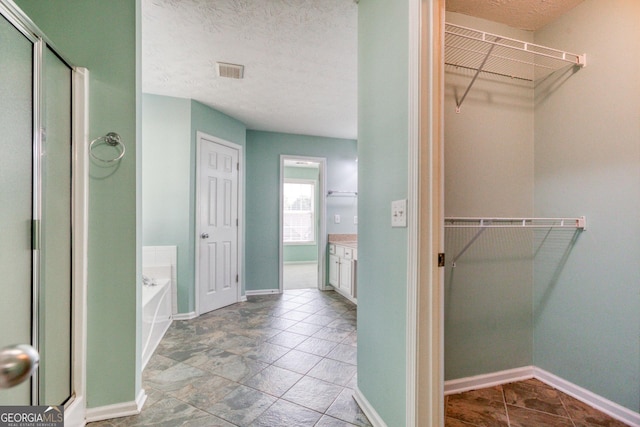 bathroom featuring a textured ceiling, vanity, visible vents, a bath, and a walk in closet